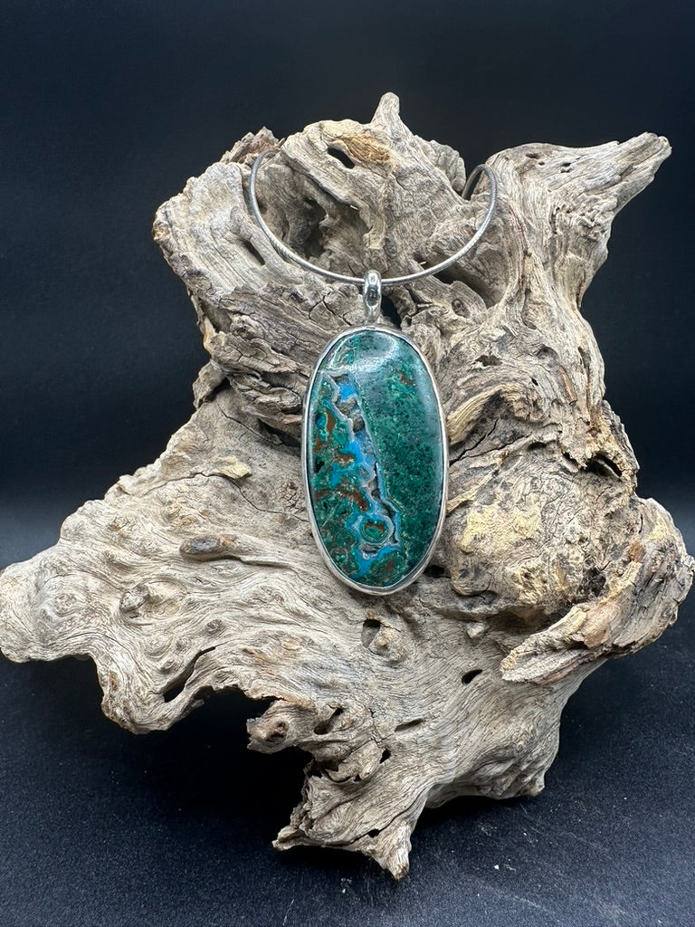 Pendant with a green and blue pattern on a piece of driftwood against a dark background