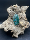 Pendant with a green and blue pattern on a piece of driftwood against a dark background
